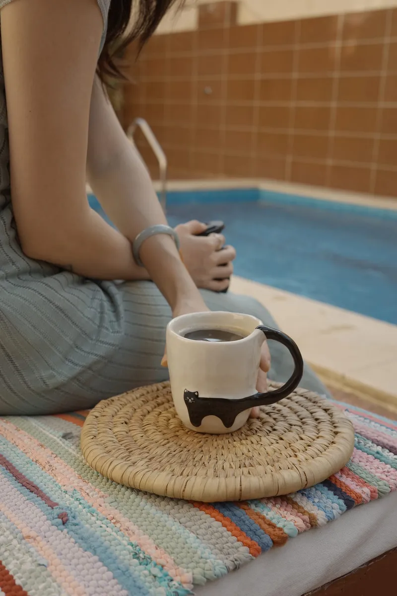 Black Cat mug on a woven mat by a pool, seen from the side