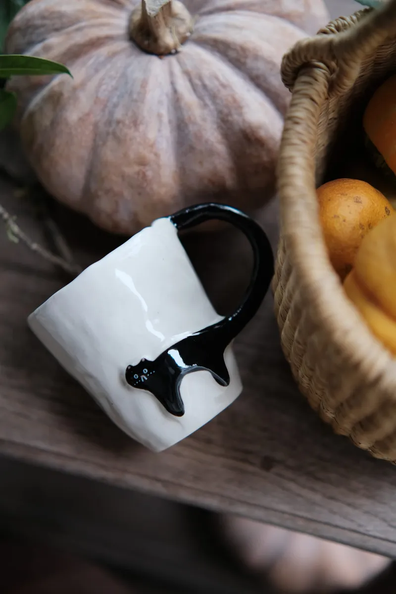 Black Cat mug lying in a basket with a grey pumpkin and small oranges