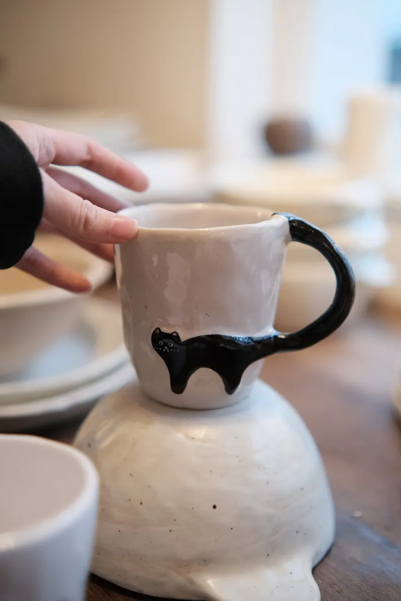Close-up of the black cat and tail handle on a milk-white mug