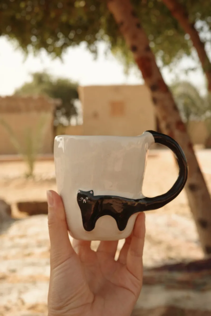 Black Cat mug held in a hand under a tree in bright sunlight