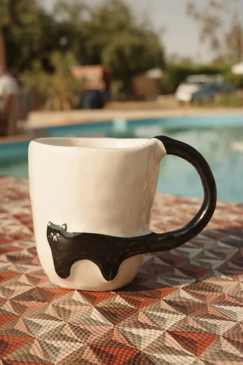 Black Cat mug on a patterned tablecloth by a pool