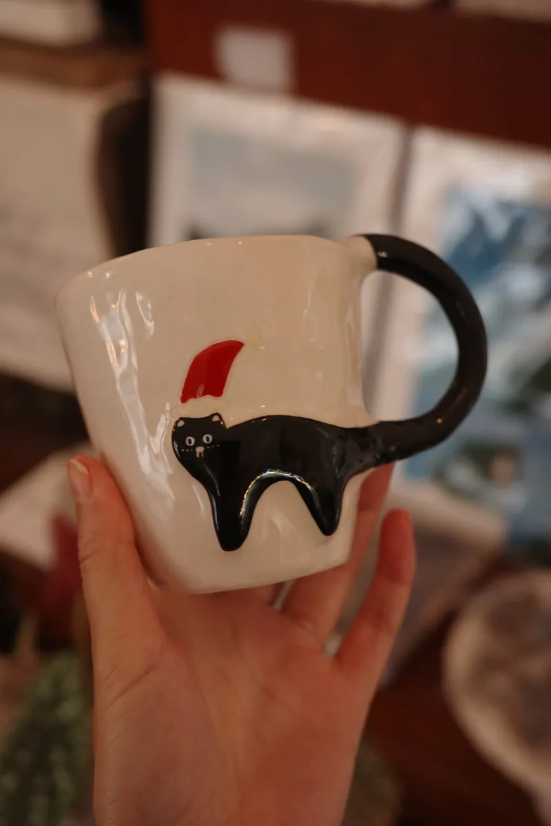Hand holding the Christmas black cat mug, red wall blurred behind
