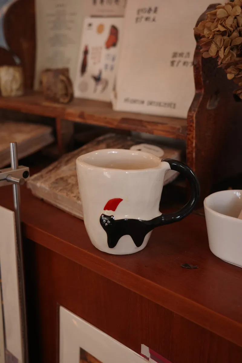Christmas black cat mug on a shop counter with books and dried flowers