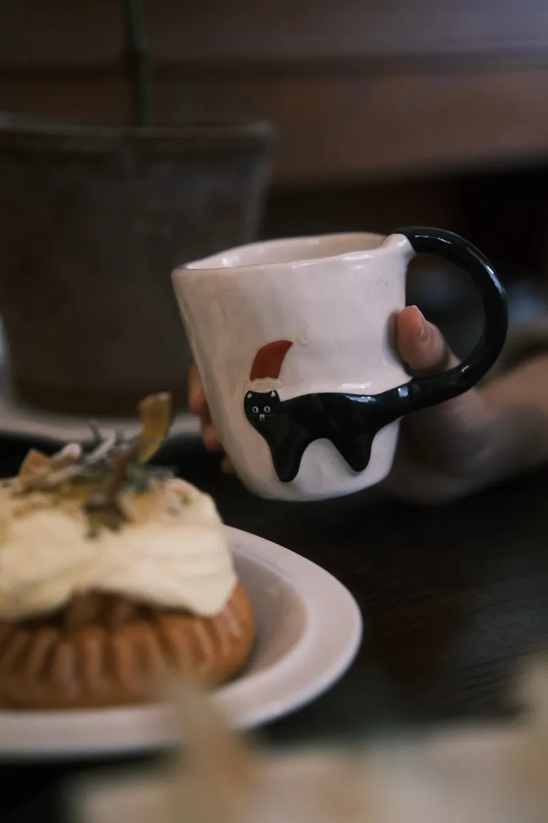 Christmas black cat mug held in a cafe with a tart in the foreground