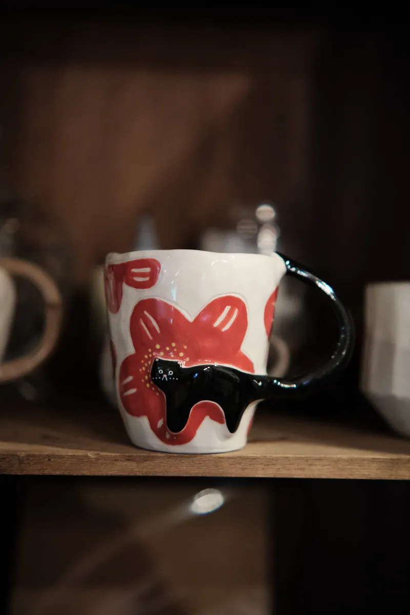 Black cat and red flowers mug on a dark wooden shelf