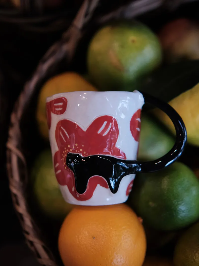 Red flowers, yellow centres and the black cat, mug resting on oranges in a basket