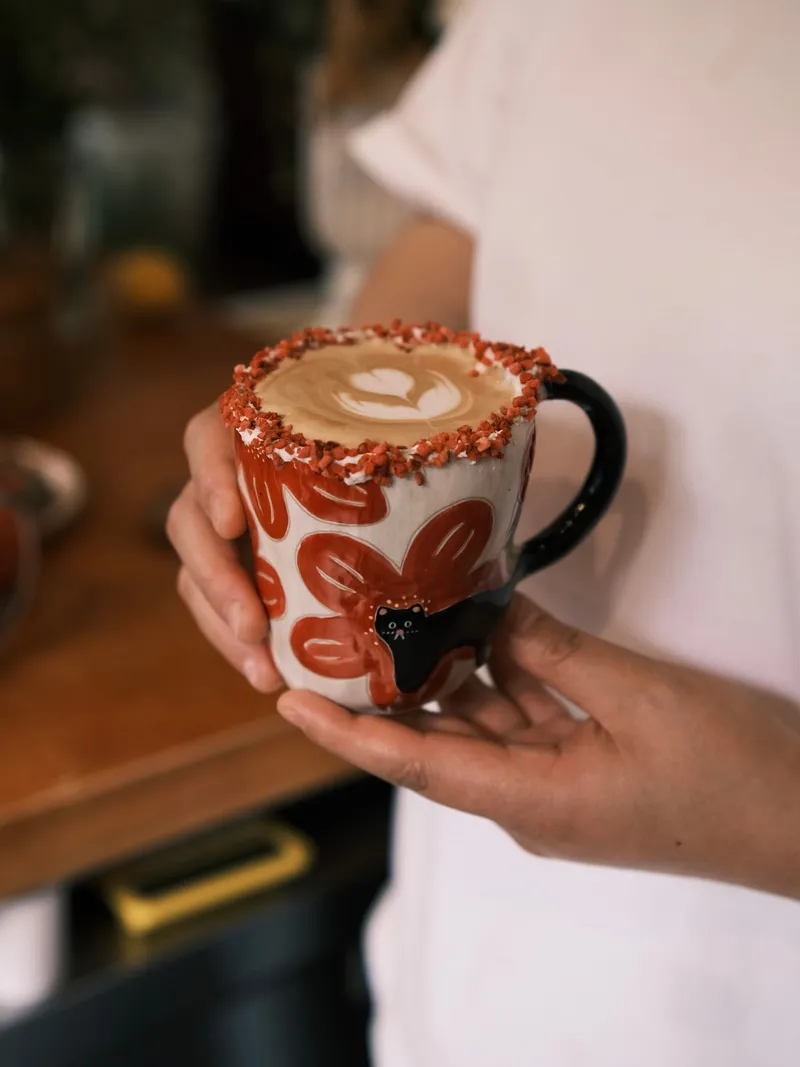 Two hands holding the red flowers mug filled with latte art