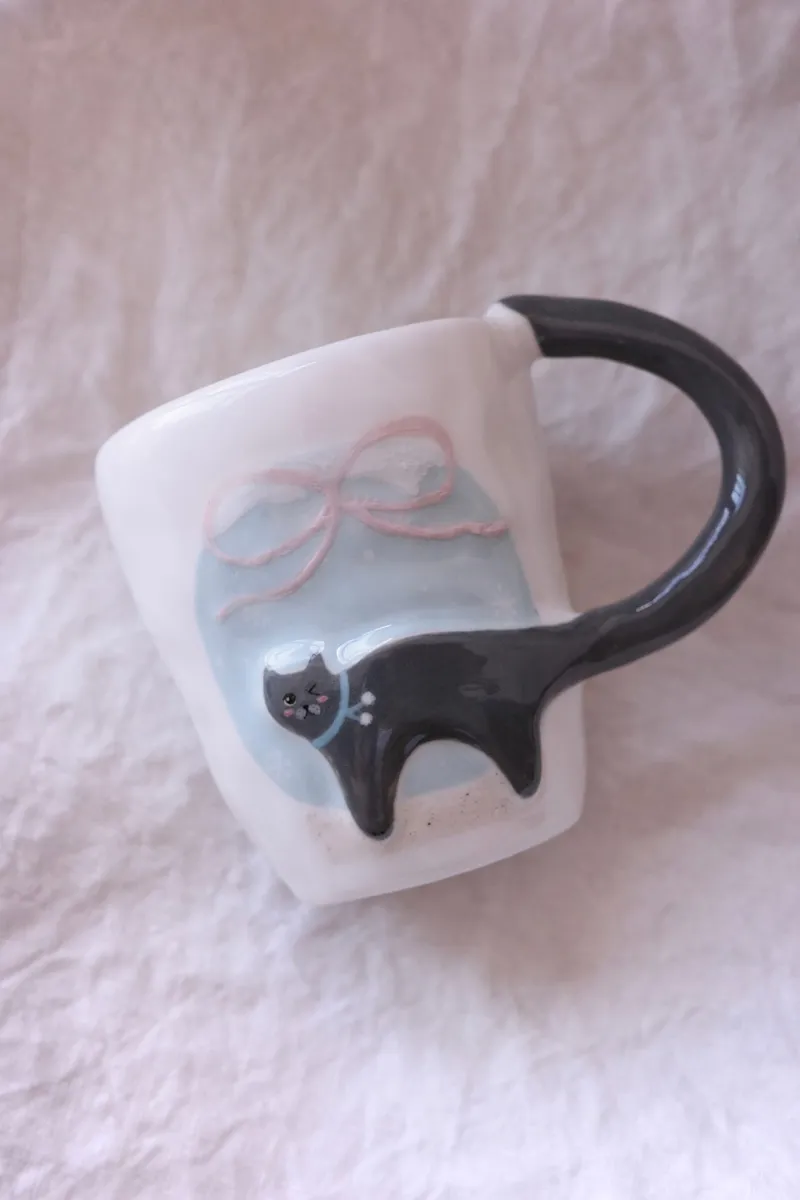 Blue-grey cat mug with a pink bow and blue sky on white linen