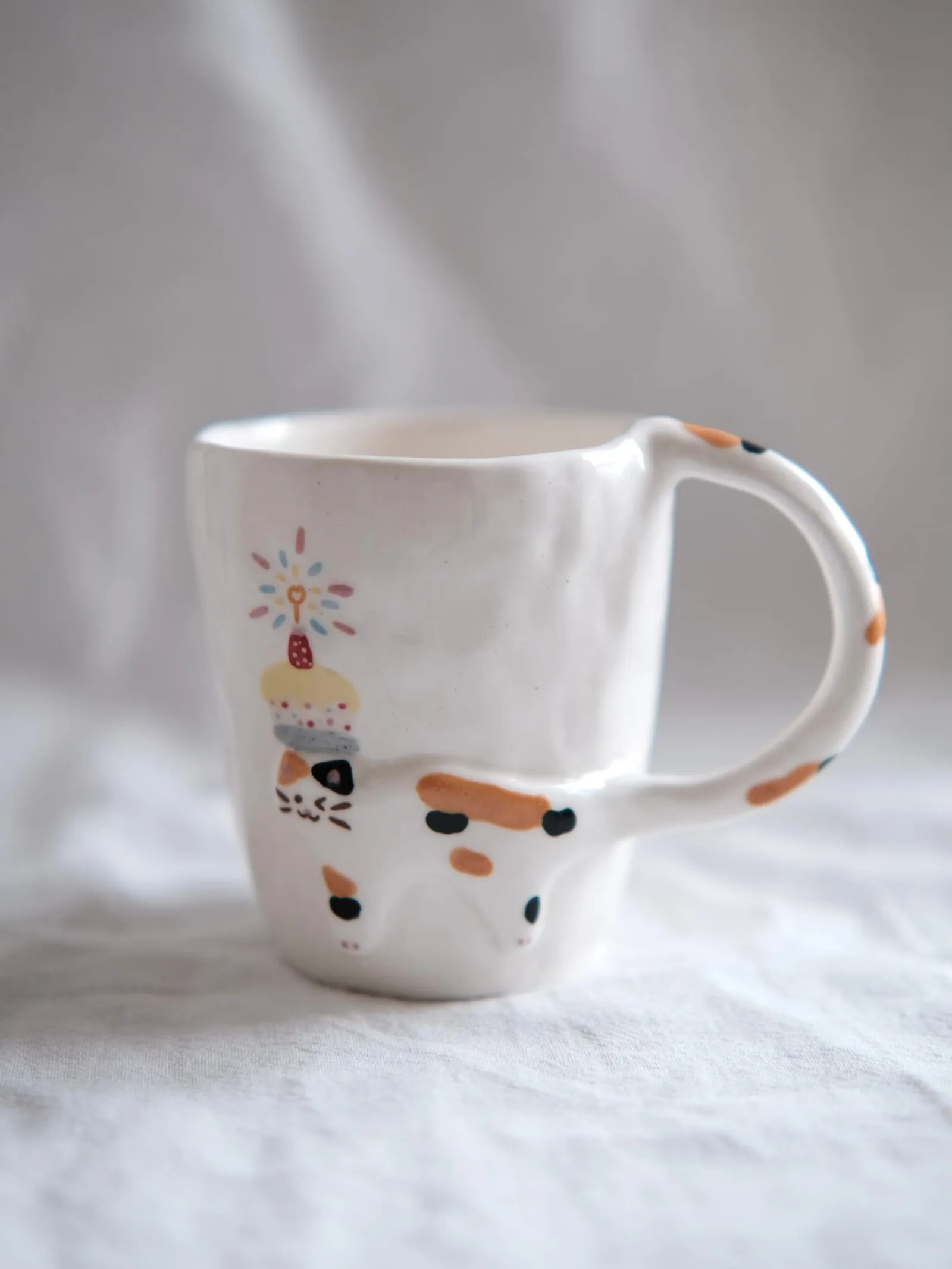 Calico cat mug with a painted birthday cake on white linen