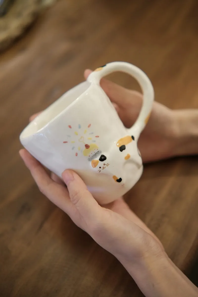 Calico birthday mug held in one hand over a wooden table