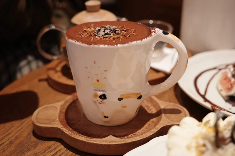 Calico birthday mug with hot chocolate on a wooden tray beside a cake