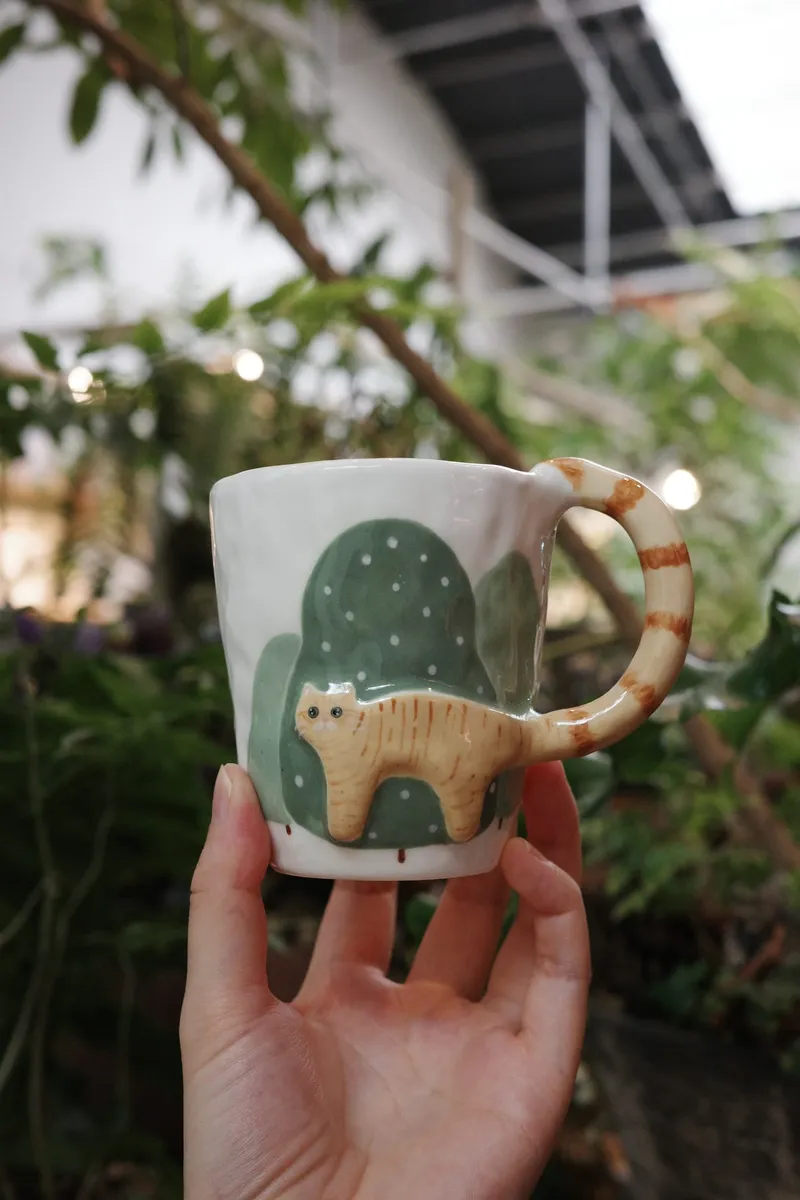 Orange cat mug held up in a greenhouse