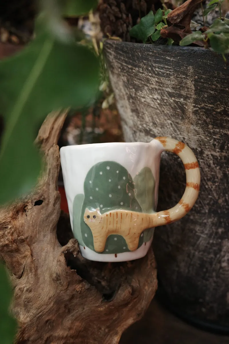 Orange cat mug on driftwood, tail handle striped like a tabby