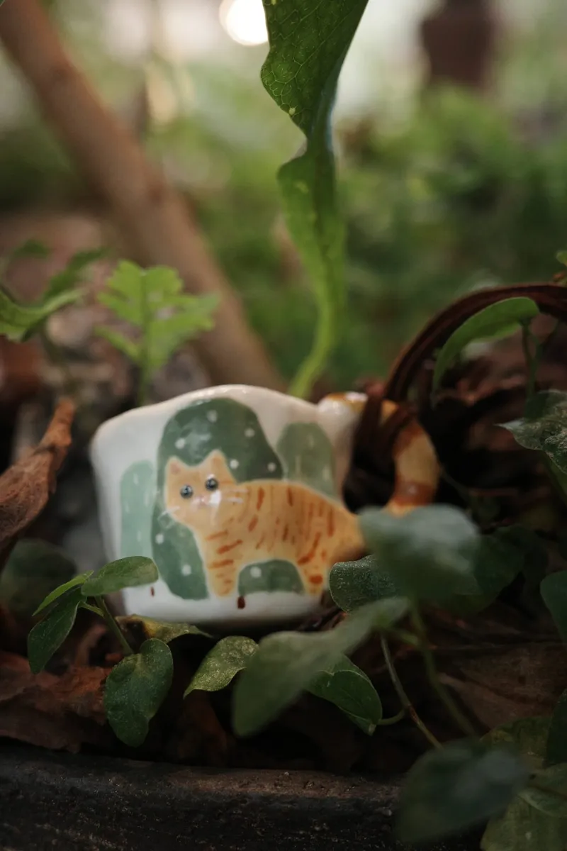 Orange cat mug among green leaves