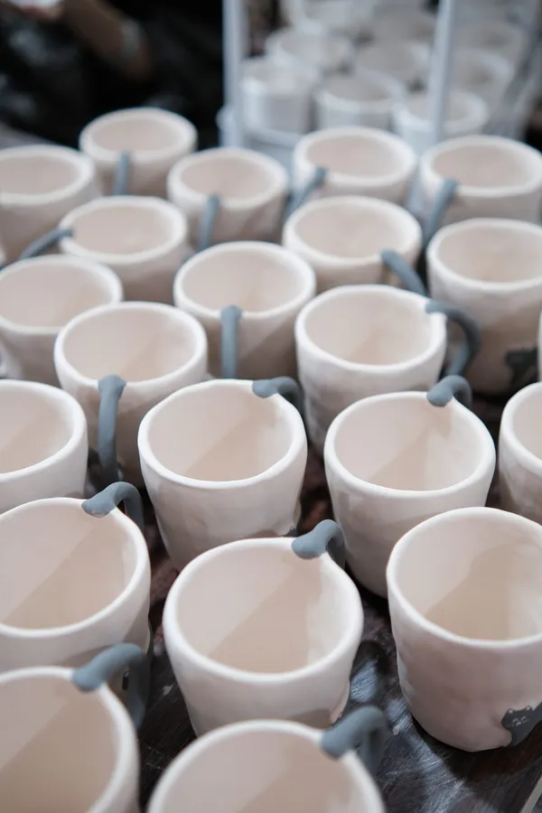Rows of unfired mugs drying on a studio cart