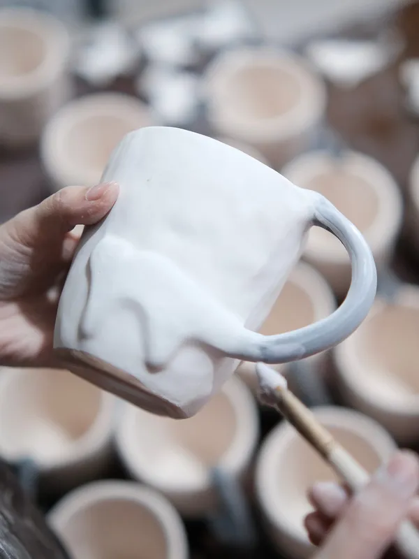 A hand holding a freshly built mug before firing
