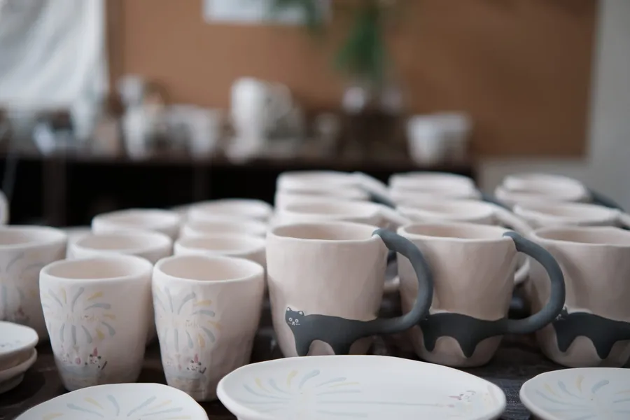 A table of unfired cat mugs waiting for the kiln