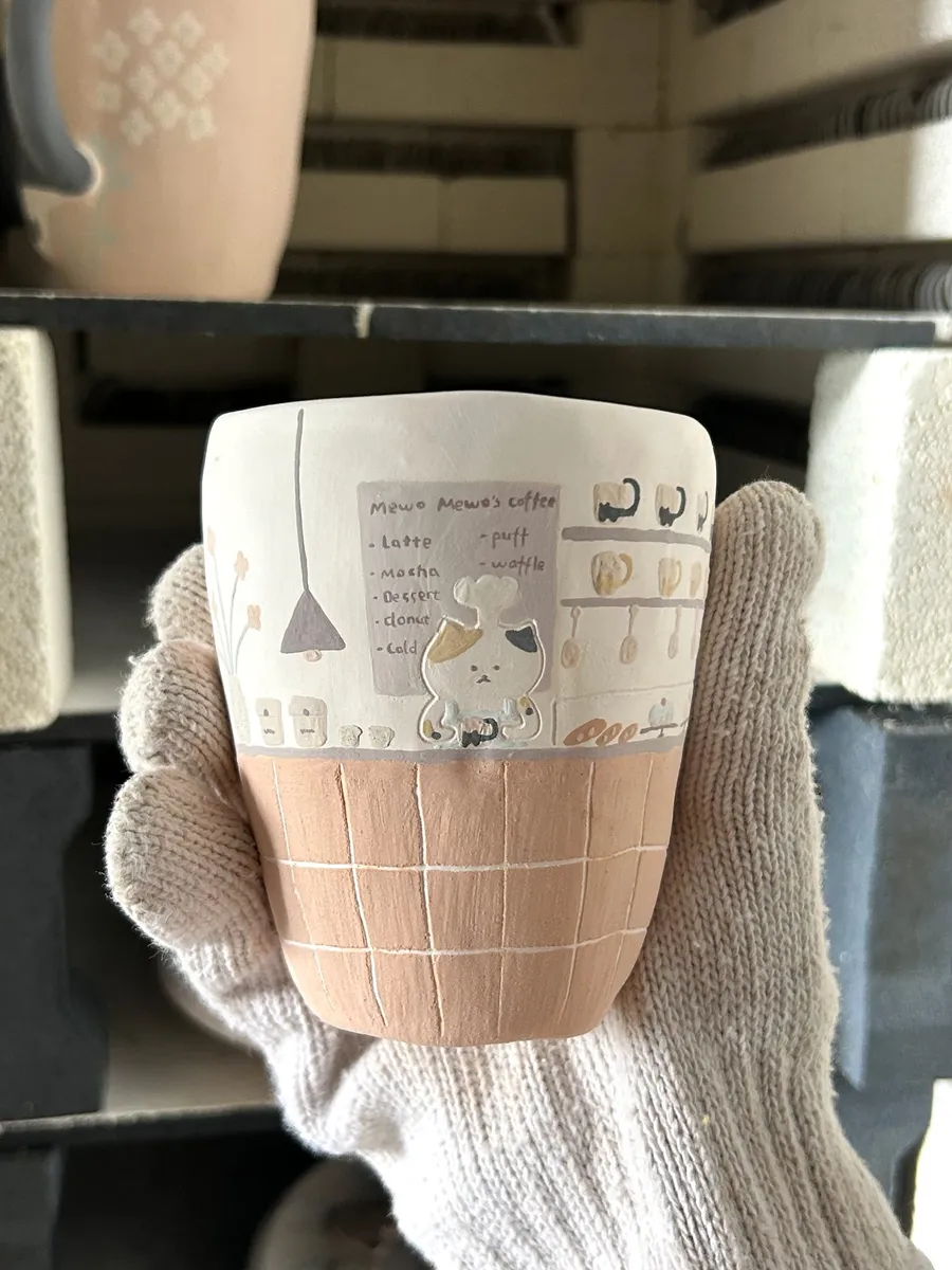 Gloved hand lifting a mug out of the kiln
