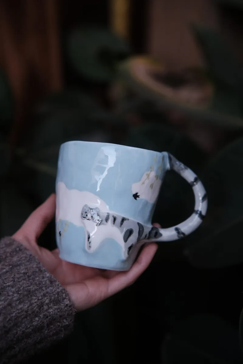 Tabby cat mug held in one hand in a garden