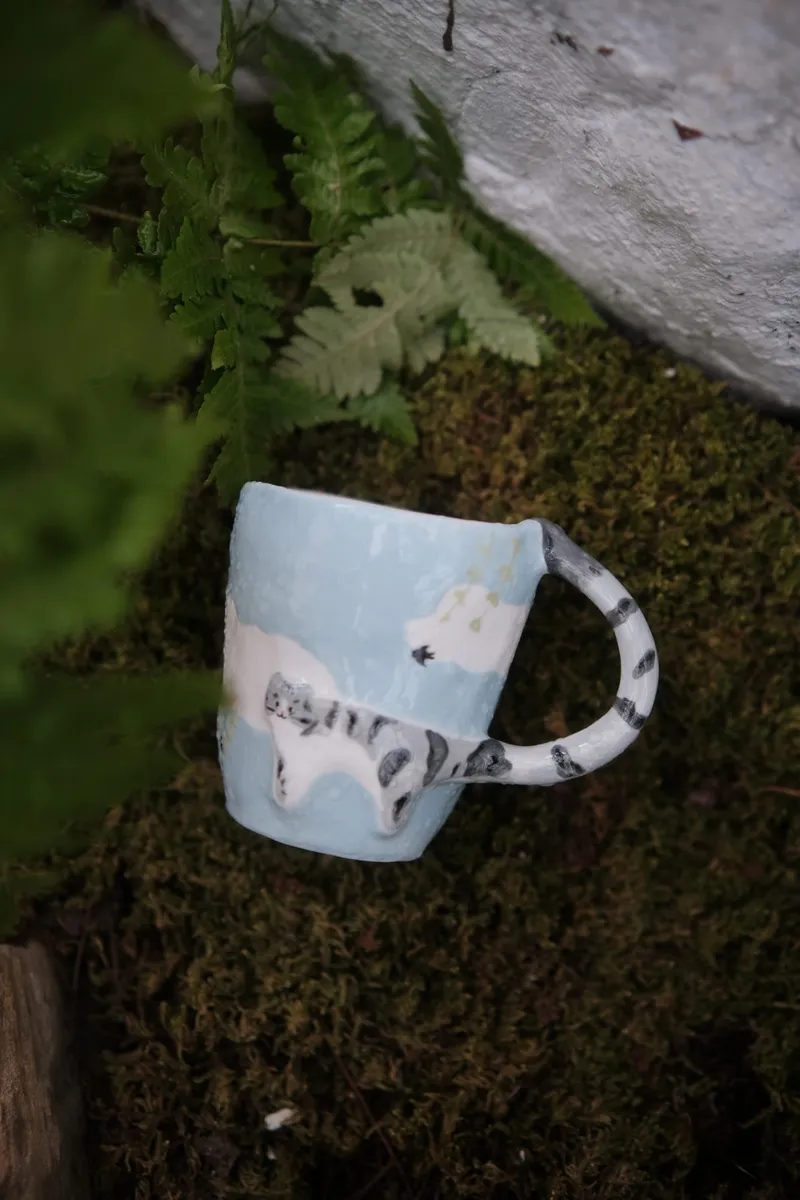 Tabby cat mug on mossy stone among ferns